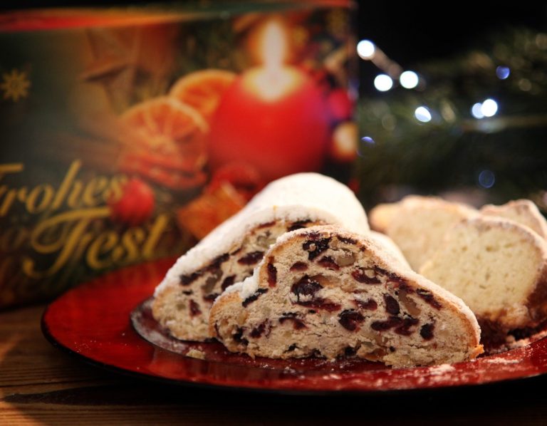 Stollen mit weihnachtlicher Verpackung Gedeckter Weihnachtsteller mit Cranberry-Walnuss-Stollen, einem Stück Mandelstollen und Geschenkverpackung im Hintergrund